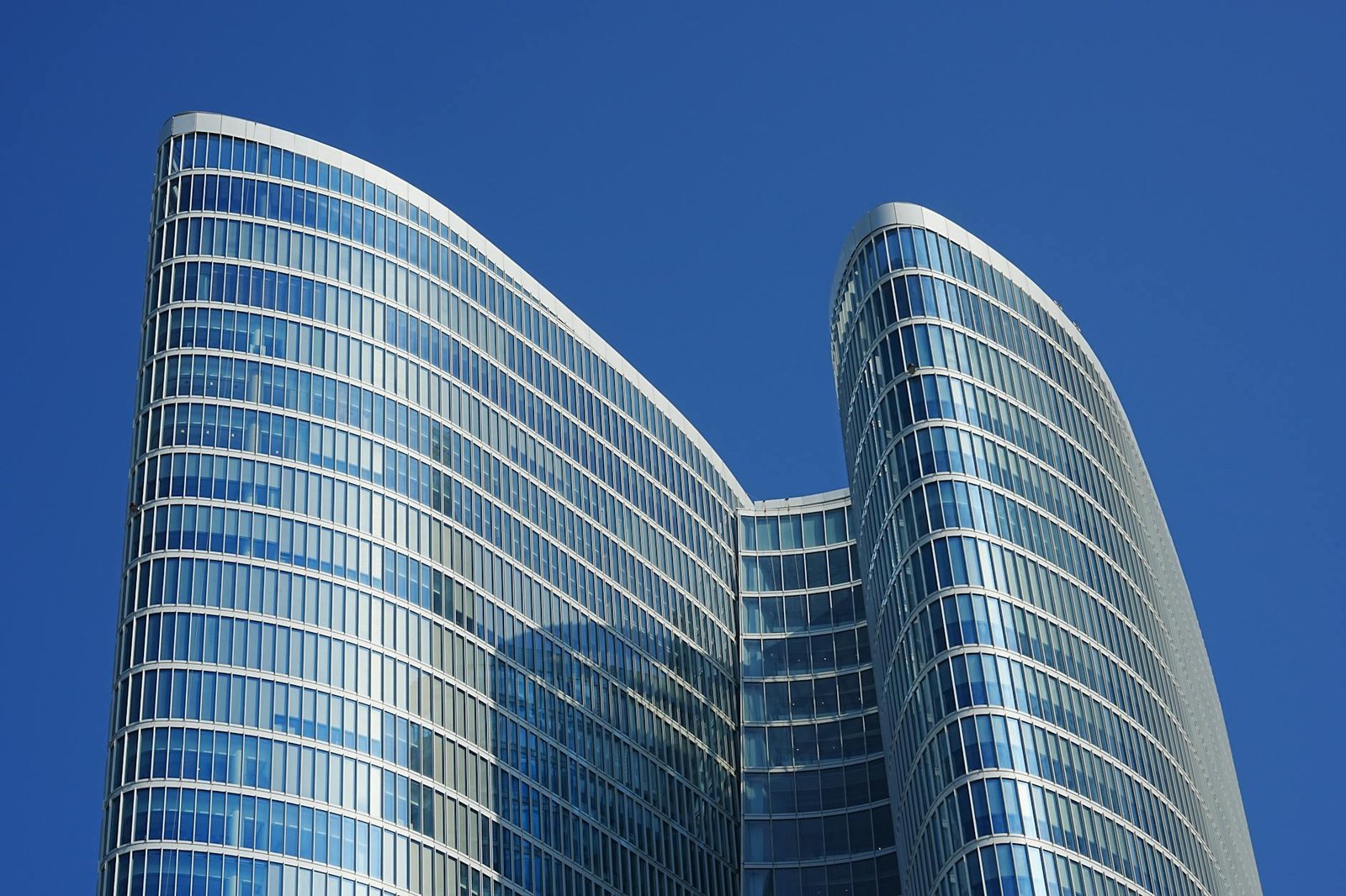 Architectural view of a sleek, modern skyscraper in Dubai with reflective glass windows against a vibrant blue sky.