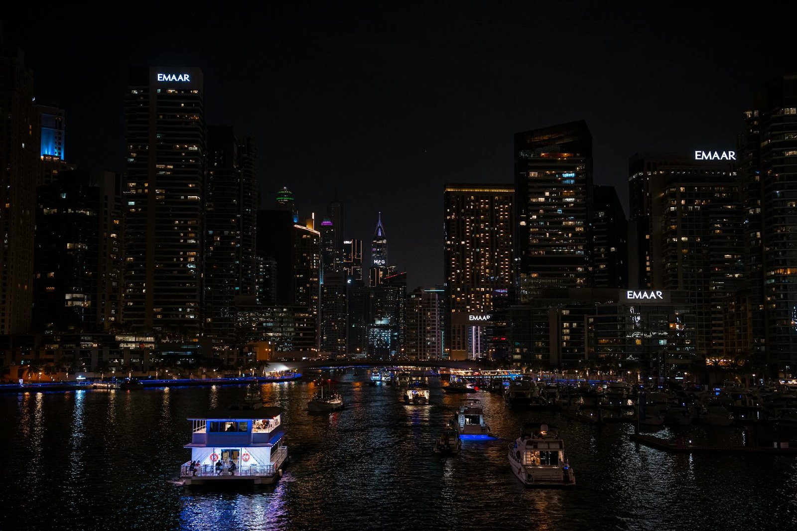 Illuminated Dubai Marina skyline at night with boats on the water.