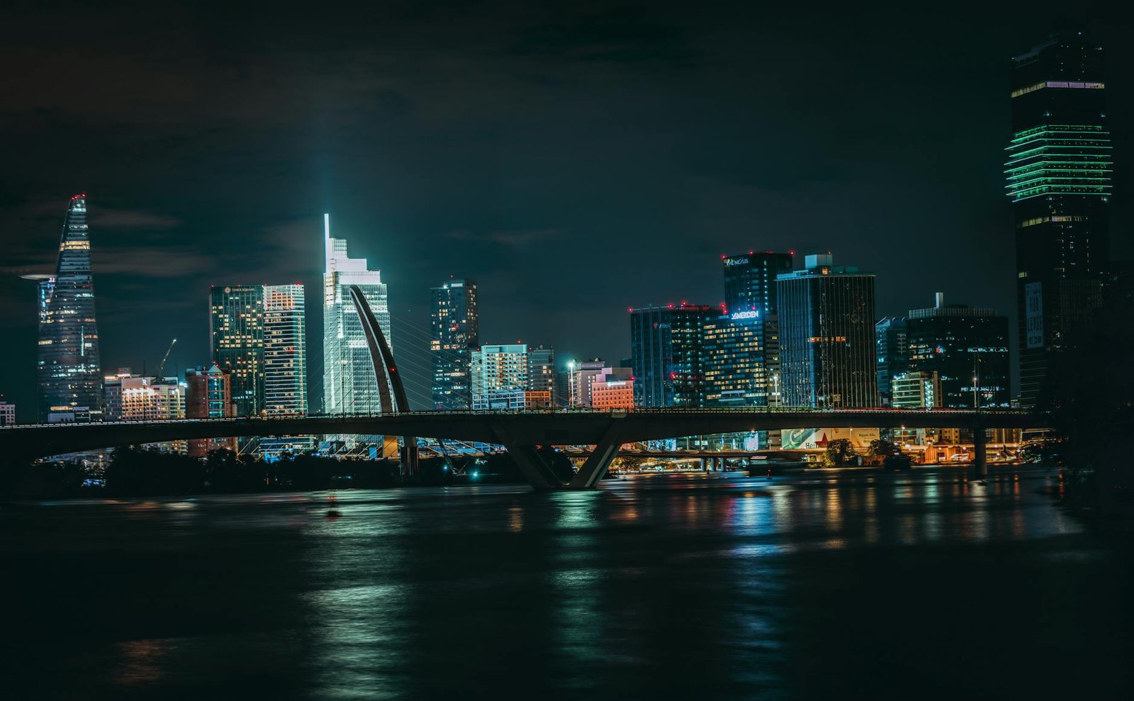 Stunning nighttime cityscape with glowing skyscrapers and a bridge reflecting on the water.
