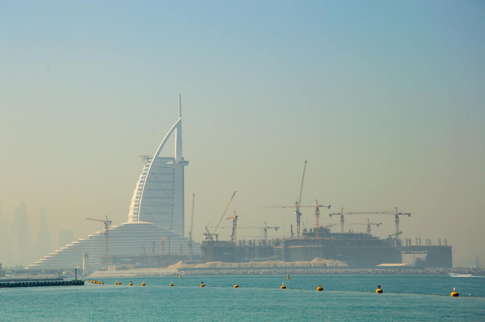 View of the Burj Al Arab and construction cranes in Dubai, showcasing urban development.