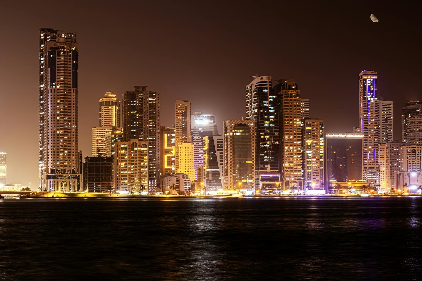 Vibrant night view of Dubai's illuminated skyline reflecting over water, showcasing modern skyscrapers.