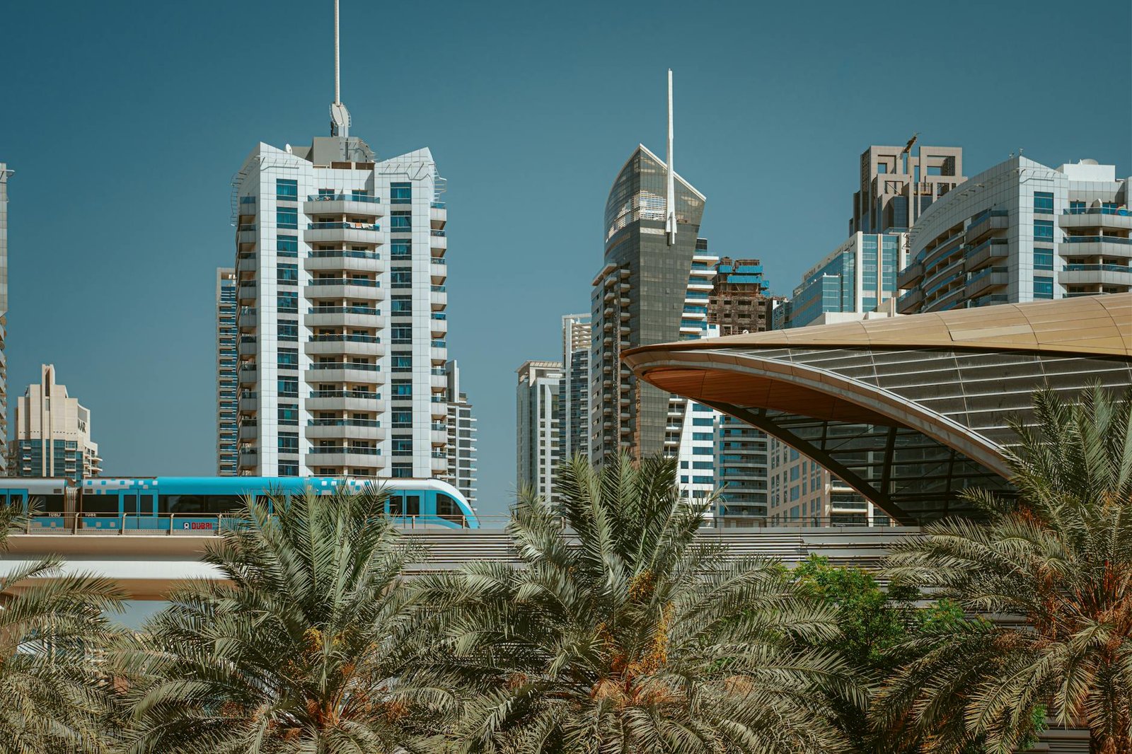Futuristic Dubai skyline with metro and palm trees under a clear blue sky.