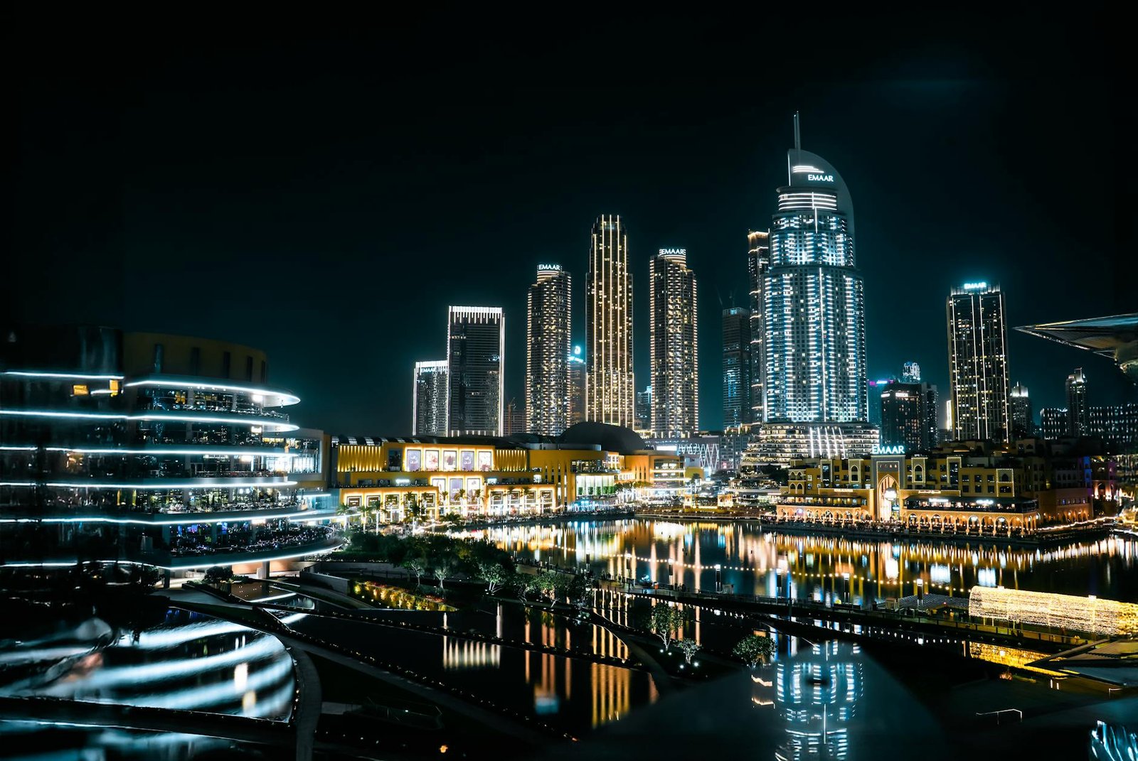 Vibrant cityscape of Dubai at night with illuminated skyscrapers reflecting on the waterfront.