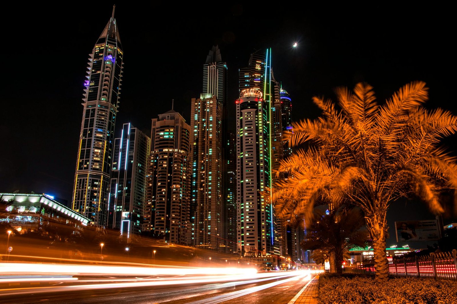 Stunning night view of Dubai's illuminated skyscrapers and palm trees with light trails from passing cars.