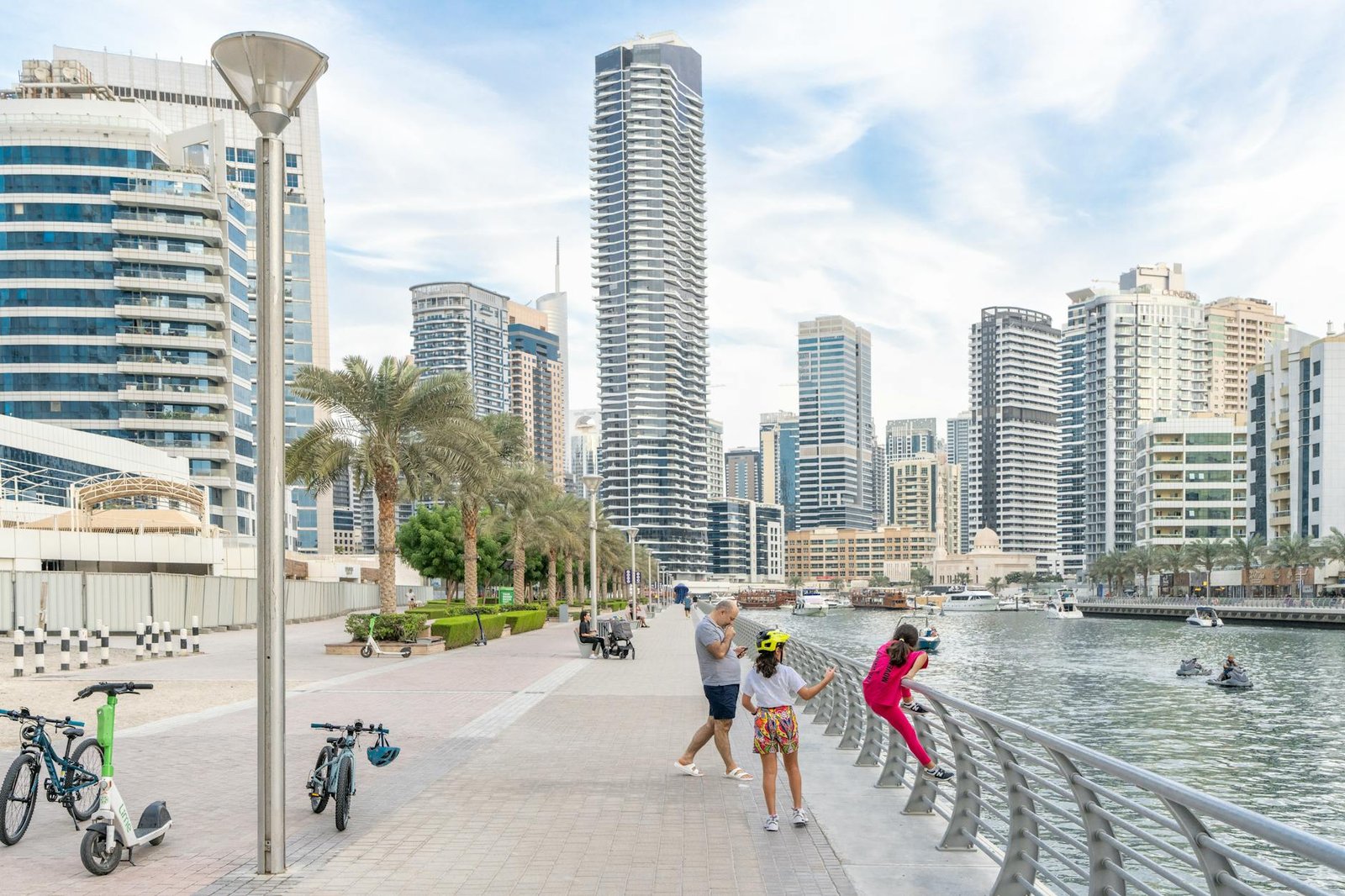 A family enjoys a walk on the Dubai Marina promenade with skyline and water views.